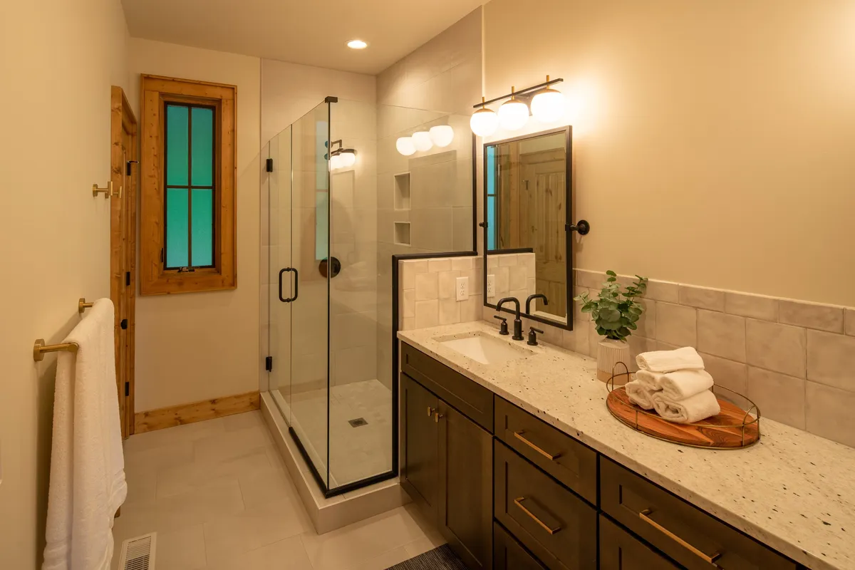 A bright, modern bathroom with a glass-enclosed shower, vanity with a framed mirror, and warm wooden accents. The scene feels clean, serene, and thoughtfully designed for daily routines or winding down at night.
