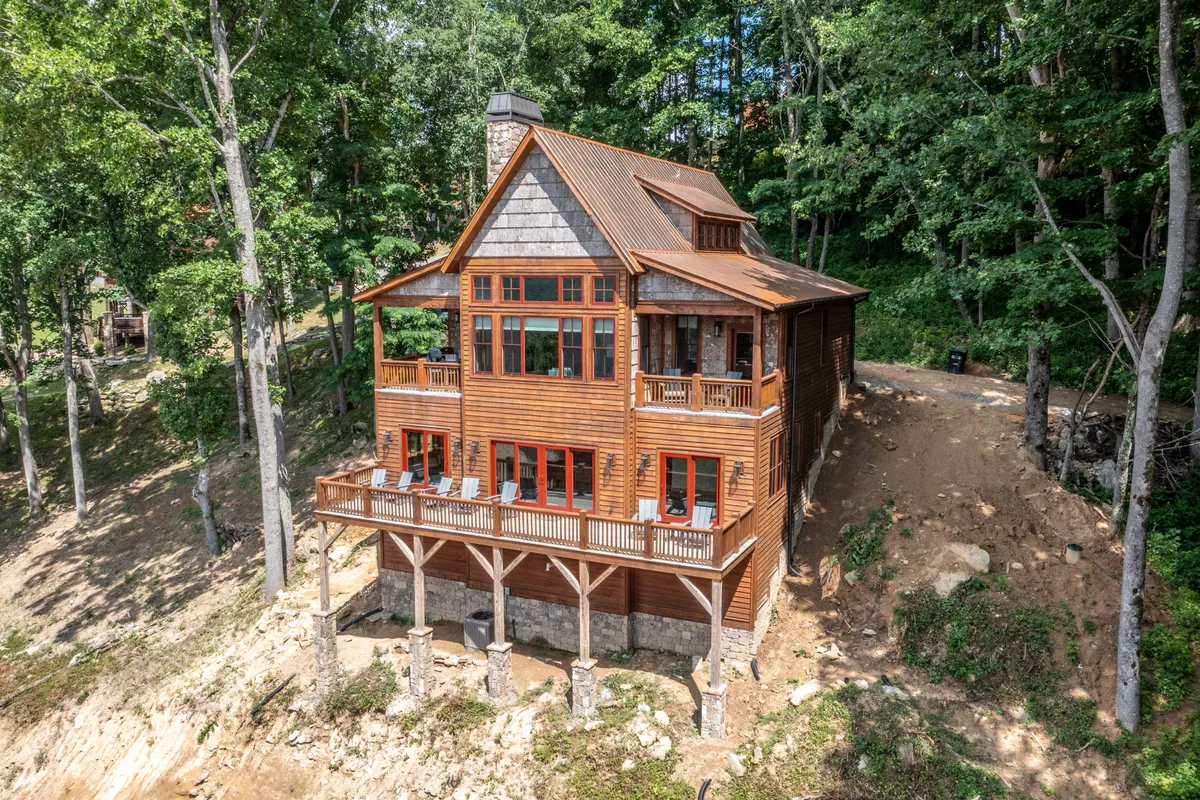 This photo depicts a serene view of the home’s wooden deck surrounded by trees, with large windows reflecting nature. The spacious deck offers an inviting setting for family gatherings, outdoor relaxation, and group games, connecting the home to its natural surroundings and providing a perfect space for evening firepit gatherings or daytime adventures.
