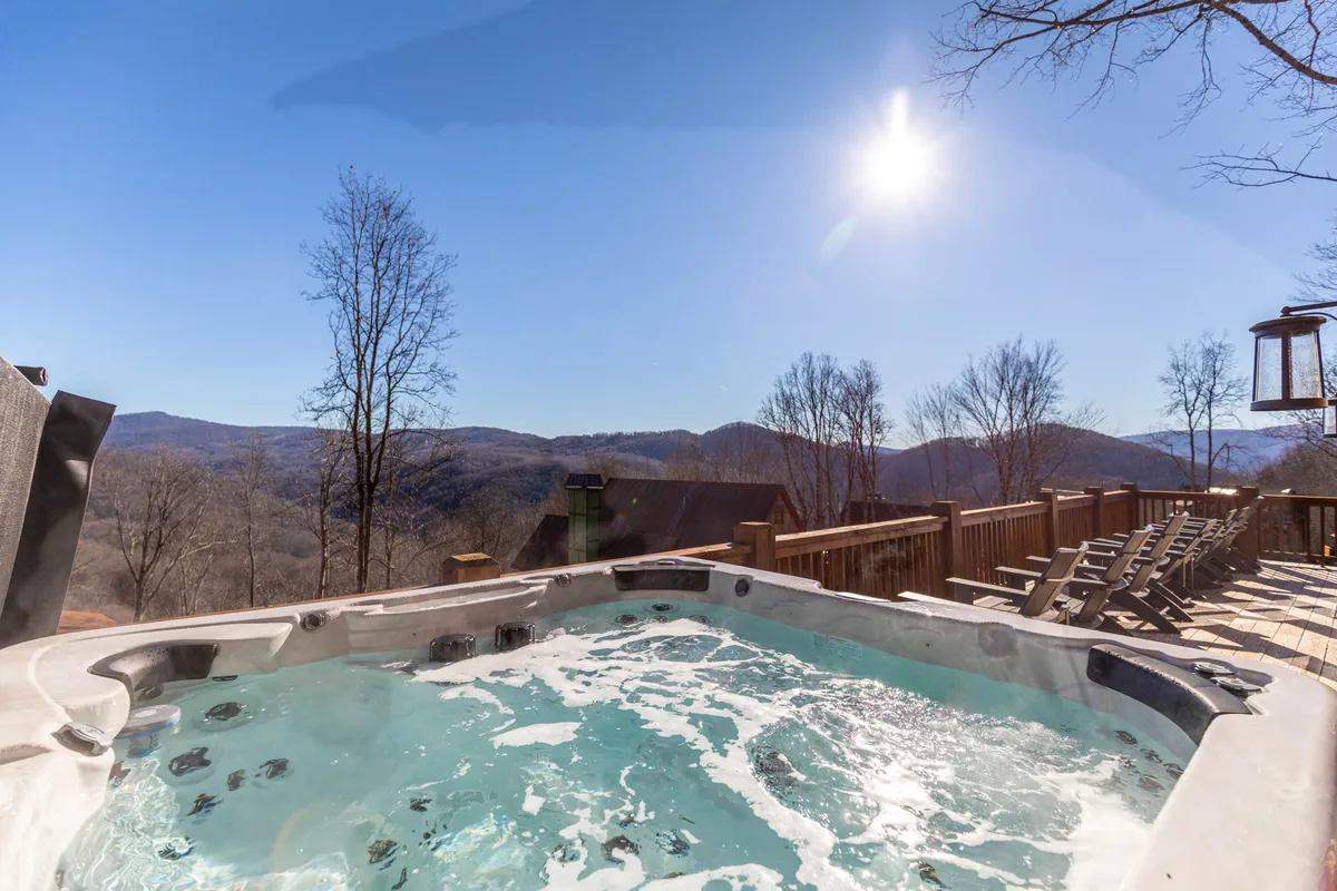 A luxurious hot tub sits on a deck overlooking majestic mountain scenery, bathed in natural sunlight. The setting radiates relaxation and the exclusive resort-style experience promised by Eagles Nest.