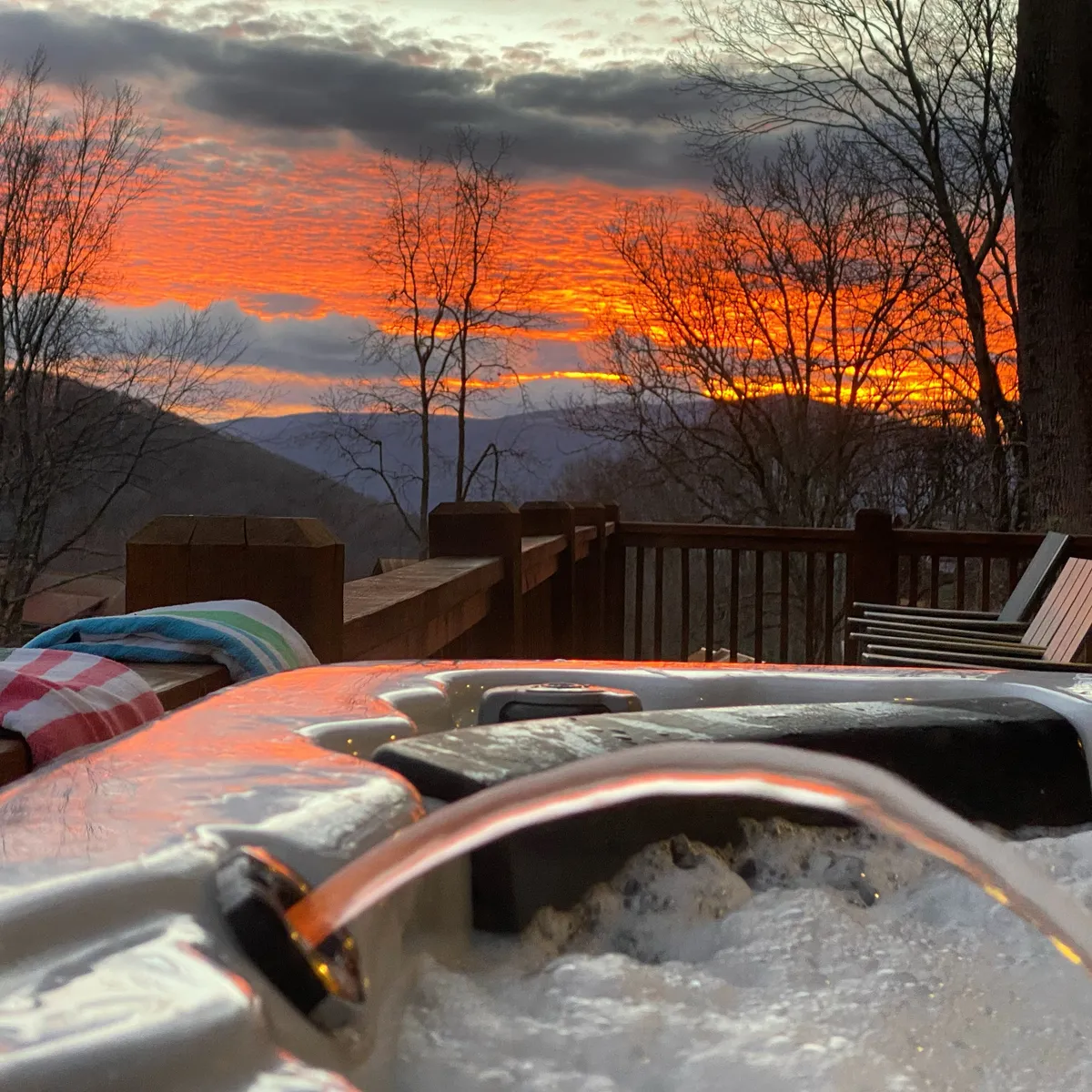 This image highlights a luxurious hot tub set on a spacious deck, overlooking a dramatic mountain sunset. The bubbling water invites relaxation, while the surrounding natural landscape provides a sense of seclusion. The deck features unobstructed views across the peaks, reinforcing the connection to the high-country outdoors.
