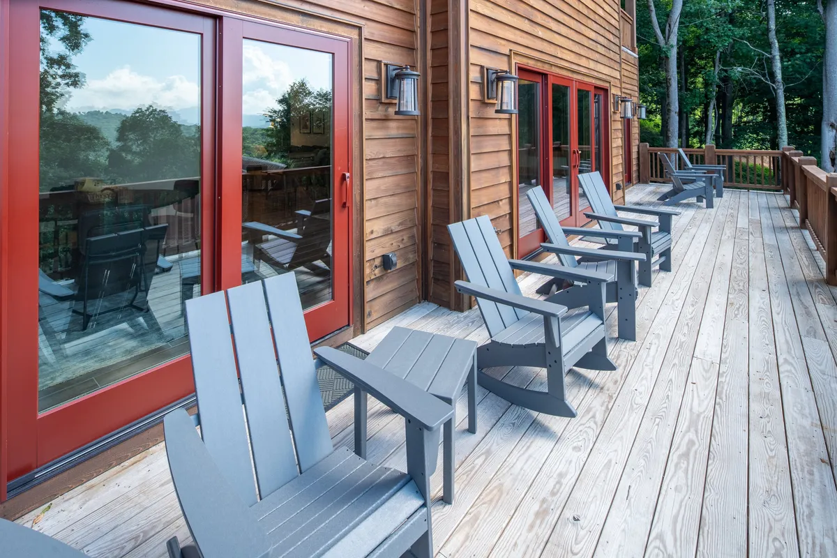 A wooden deck framed by surrounding trees, this scene includes classic Adirondack chairs and distinctive red doors. The setup is inviting for both individuals and groups to relax, socialize, and soak in the natural environment. The deck’s orientation suggests perfect positioning for sunrise or sunset views.
