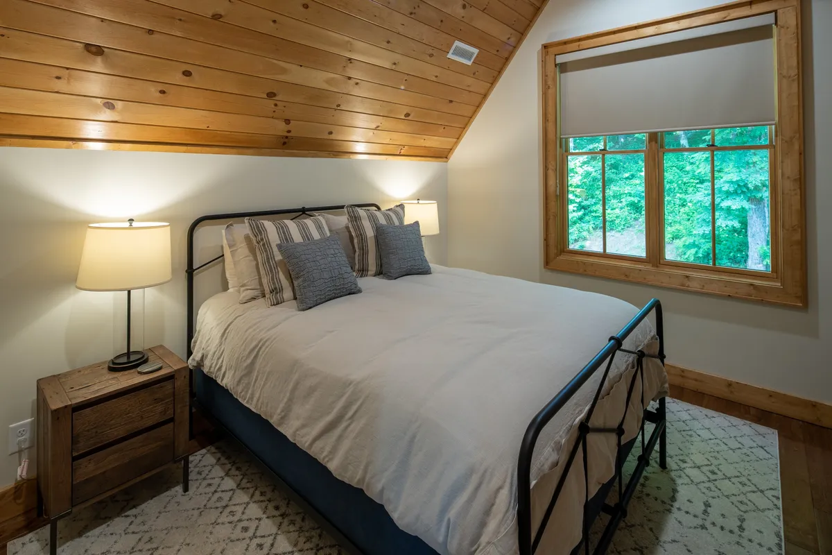 A serene bedroom featuring a comfortable bed framed by large windows, nightstands with tasteful lamps, and natural light streaming in. The decor is modern yet cozy, suggesting a restful and inviting atmosphere for unwinding at the end of the day.