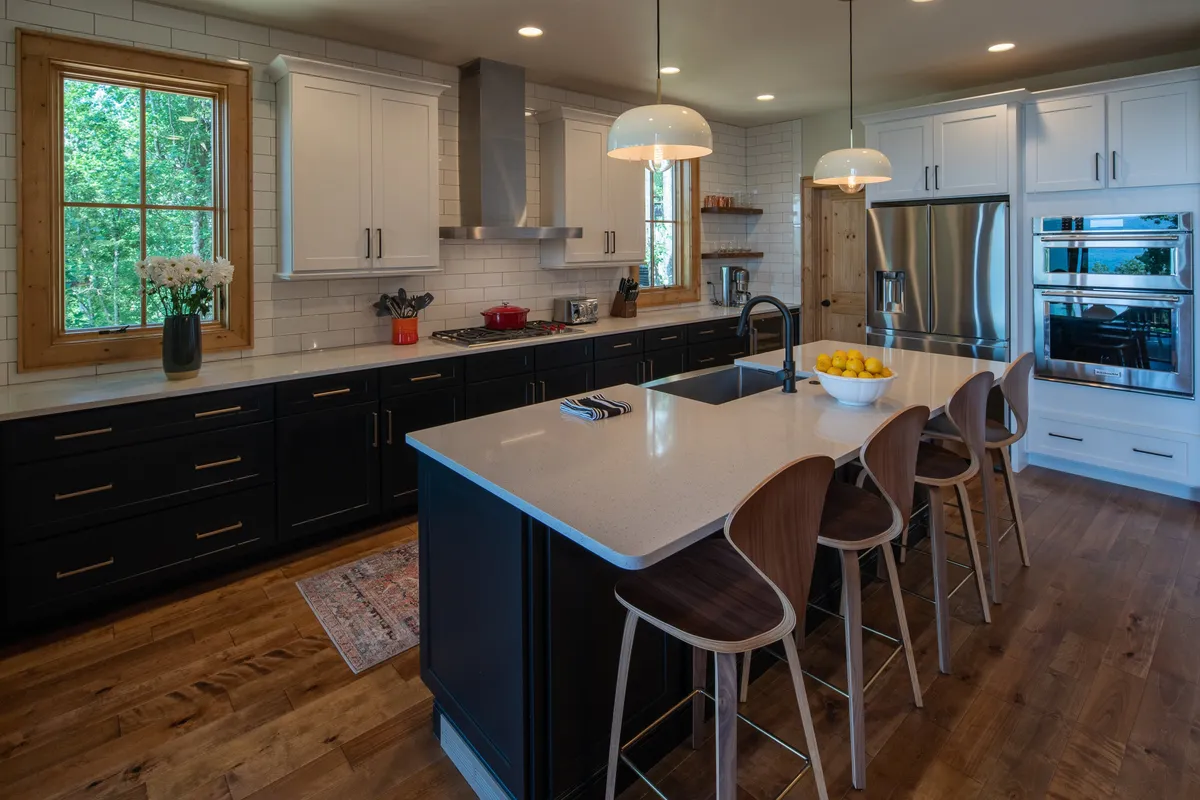 The modern kitchen is outfitted with stainless steel Dacor and Wolf appliances, a spacious central island with seating, and a large window bringing in natural light and outdoor views. The layout is designed for both culinary creativity and socializing, making it the ideal chef’s kitchen described in the section.