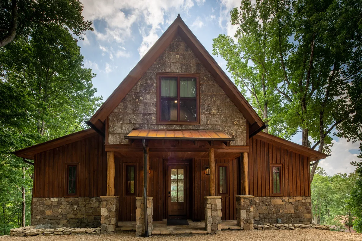 A welcoming exterior view of the property, highlighting the stone facade, wooden beams, and large windows. The front porch invites guests to relax and enjoy the surrounding nature, suggesting a warm, communal entry point for group adventures.
