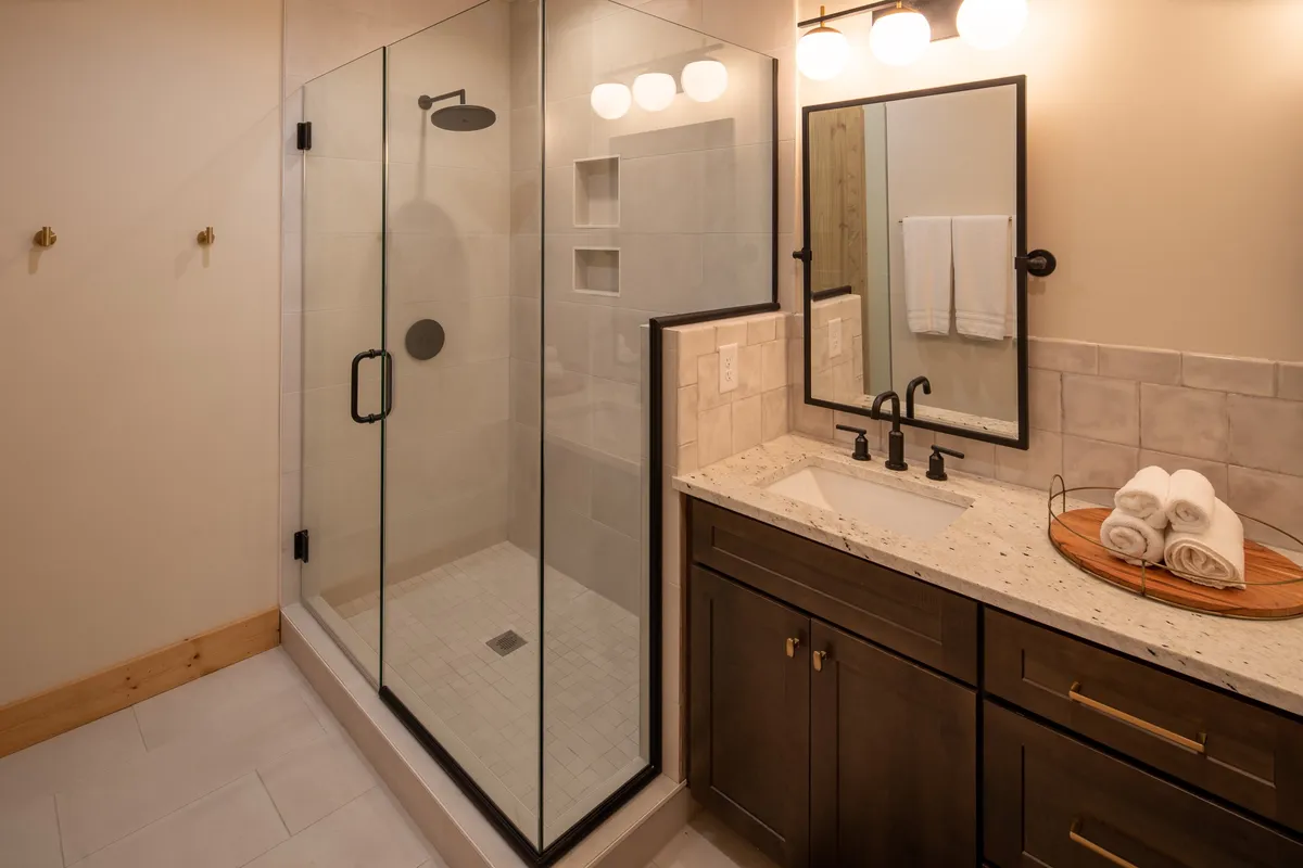 A spa-inspired bathroom featuring a glass shower enclosure, modern vanity with sink, and a decorative towel rack. The clean lines, tile surfaces, and soft lighting evoke a sense of luxury and relaxation.